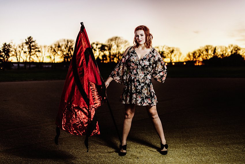 girl in a colorful dress holding a big red flag in front of a pink sunset